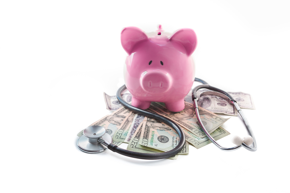 Piggy bank and stethoscope resting on pile of dollars on white background
